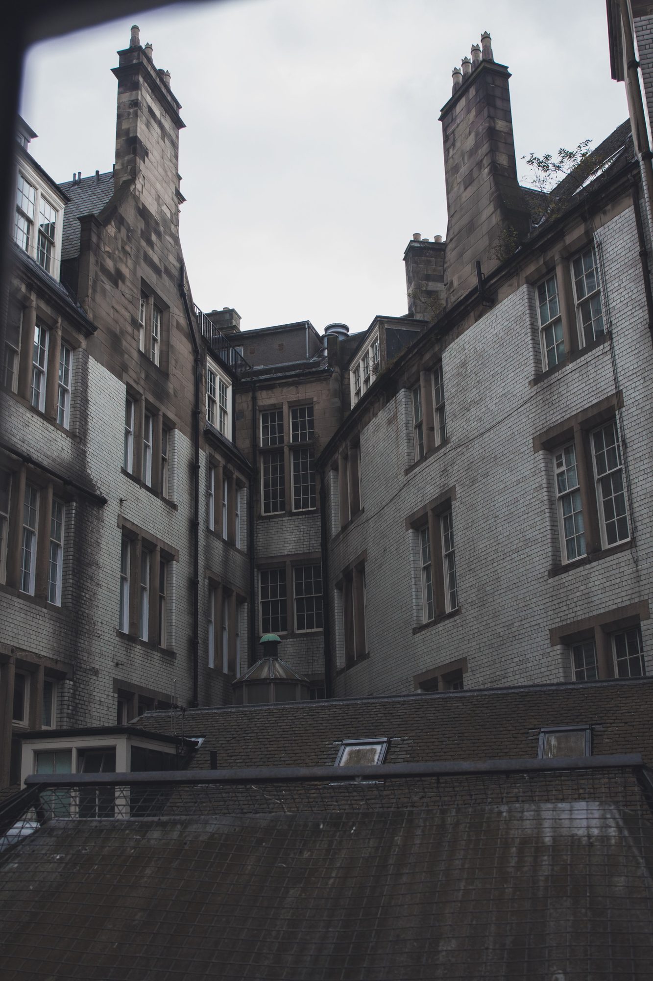An Old Town Edinburgh courtyard with two weathered, crenellated chimney stacks rising above slate roofs