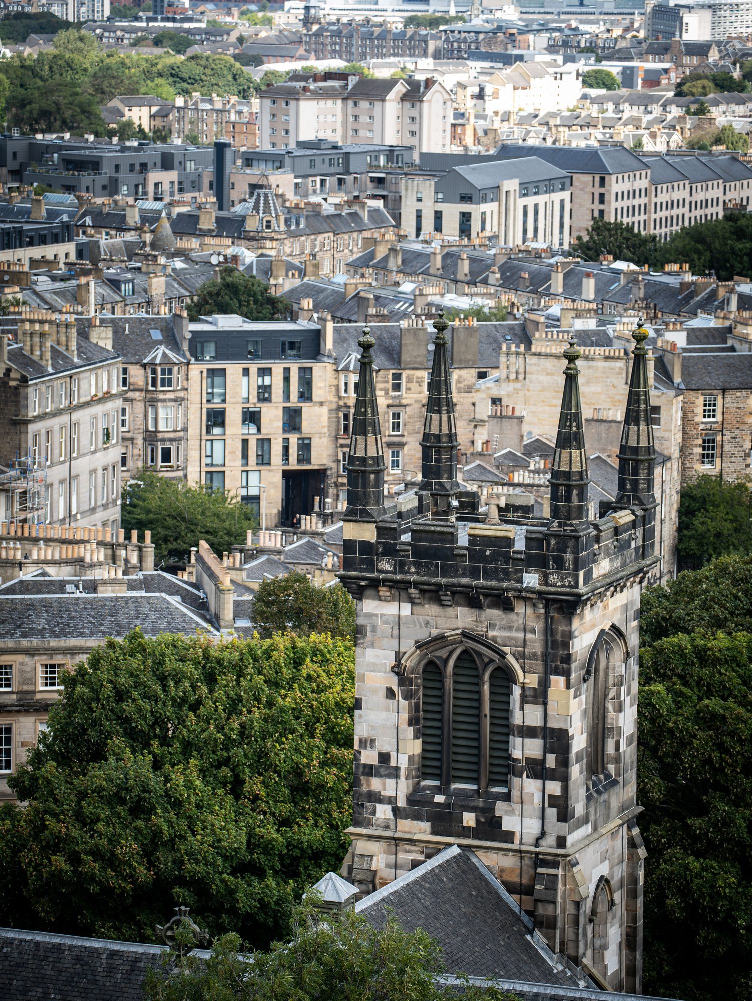 A wide Edinburgh panorama with a church spire rising above dozens of tenement chimney stacks and slate roofs
